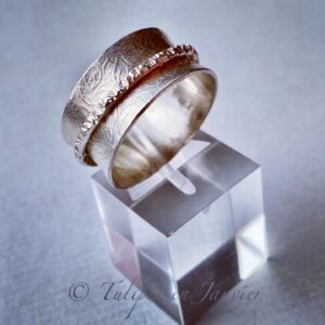 Bague large en argent avec une légère texture de feuilles. Un deuxième anneau fin avec une texture martelée est autour du premier.