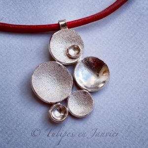 Pendentif en argent composé de cinq disques concaves de tailles variées. Trois d'entre eux ont une texture sablée et l'un d'entre eux est orné d'un petit disque concave supplémentaire.