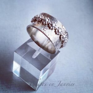 Bague en argent orné d'un léger motif de fleurs et entouré d'un anneau composé de petites fleurs.