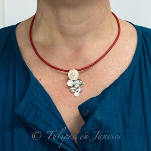 Une femme porte un pendentif en argent composé de 7 petits disques concaves sur un cordon rouge.
