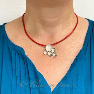 Le cou et la poitrine d'une femme portant un pendentif composé de six petits disques concaves collés les uns aux autres, le tout monté sur un cordon de cuir rouge.